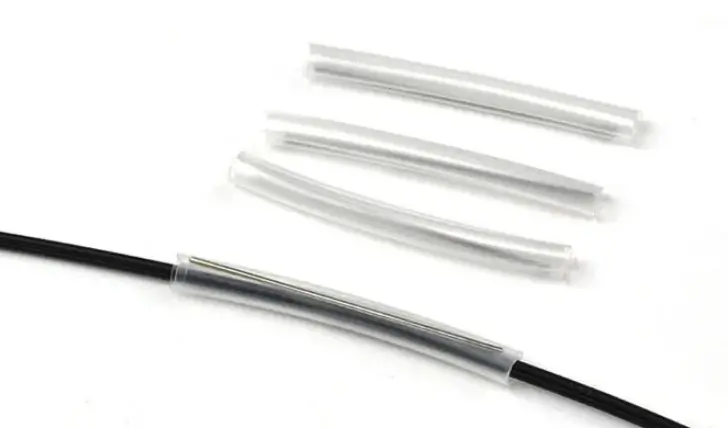 Transparent heat-shrink sleeve covers a black fiber, with spare sleeves placed behind it.