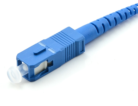 Blue SC fiber connector with a rectangular housing, latch area, and white ferrule cap at the connector end.
